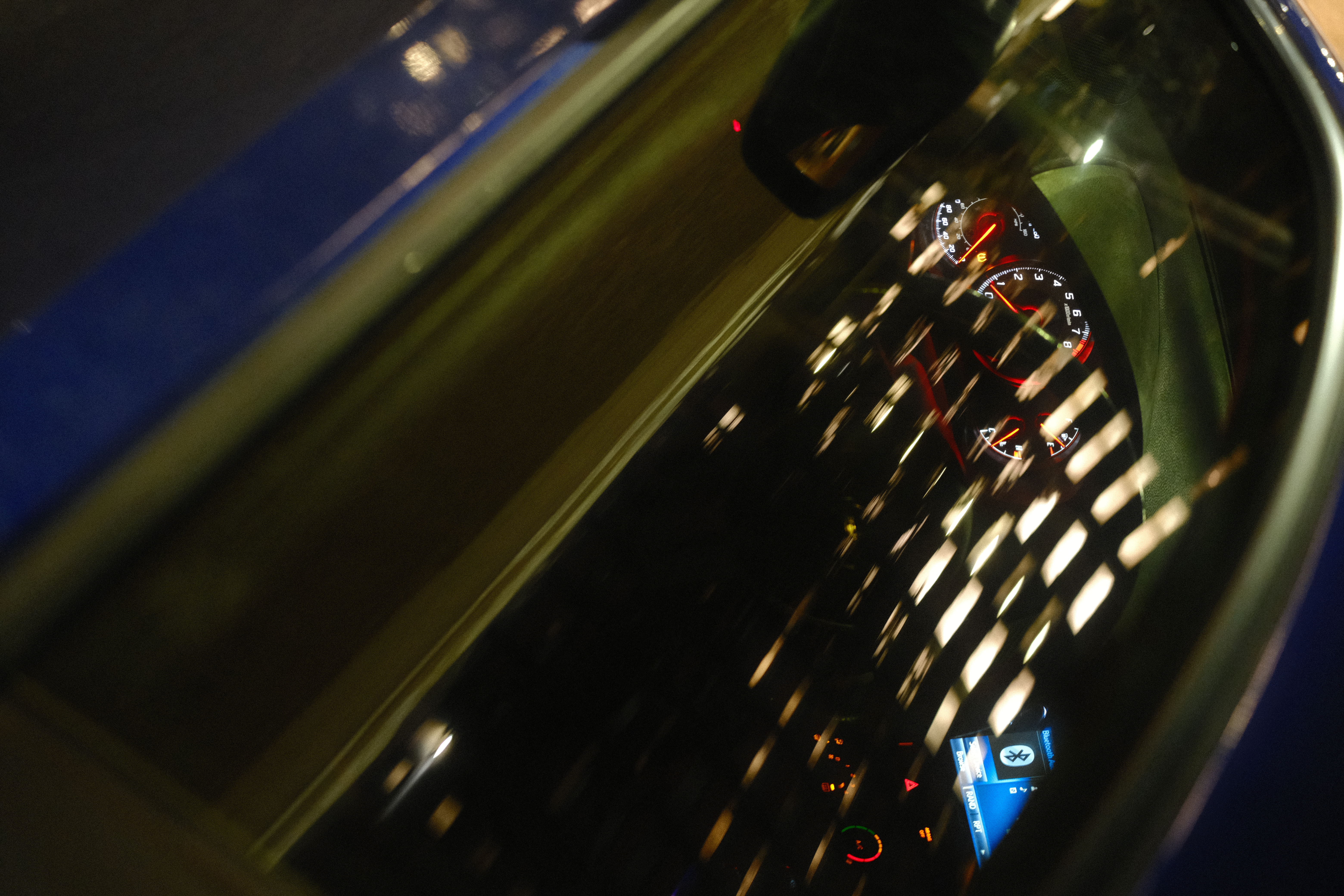 A nighttime view of a car dashboard reflected in the windshield
